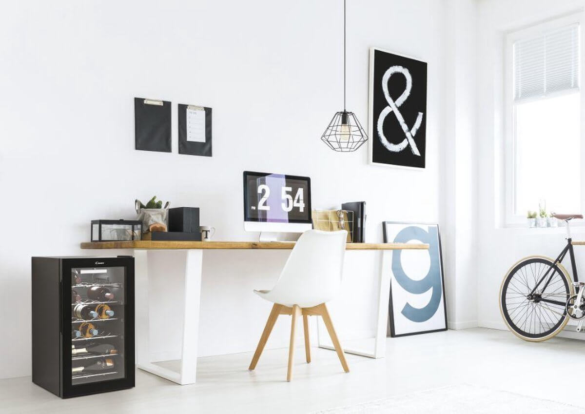 Candy CWC 021 M/N wijnkoelkast onder een houten bureau in een modern thuiskantoor, geschikt voor 21 flessen