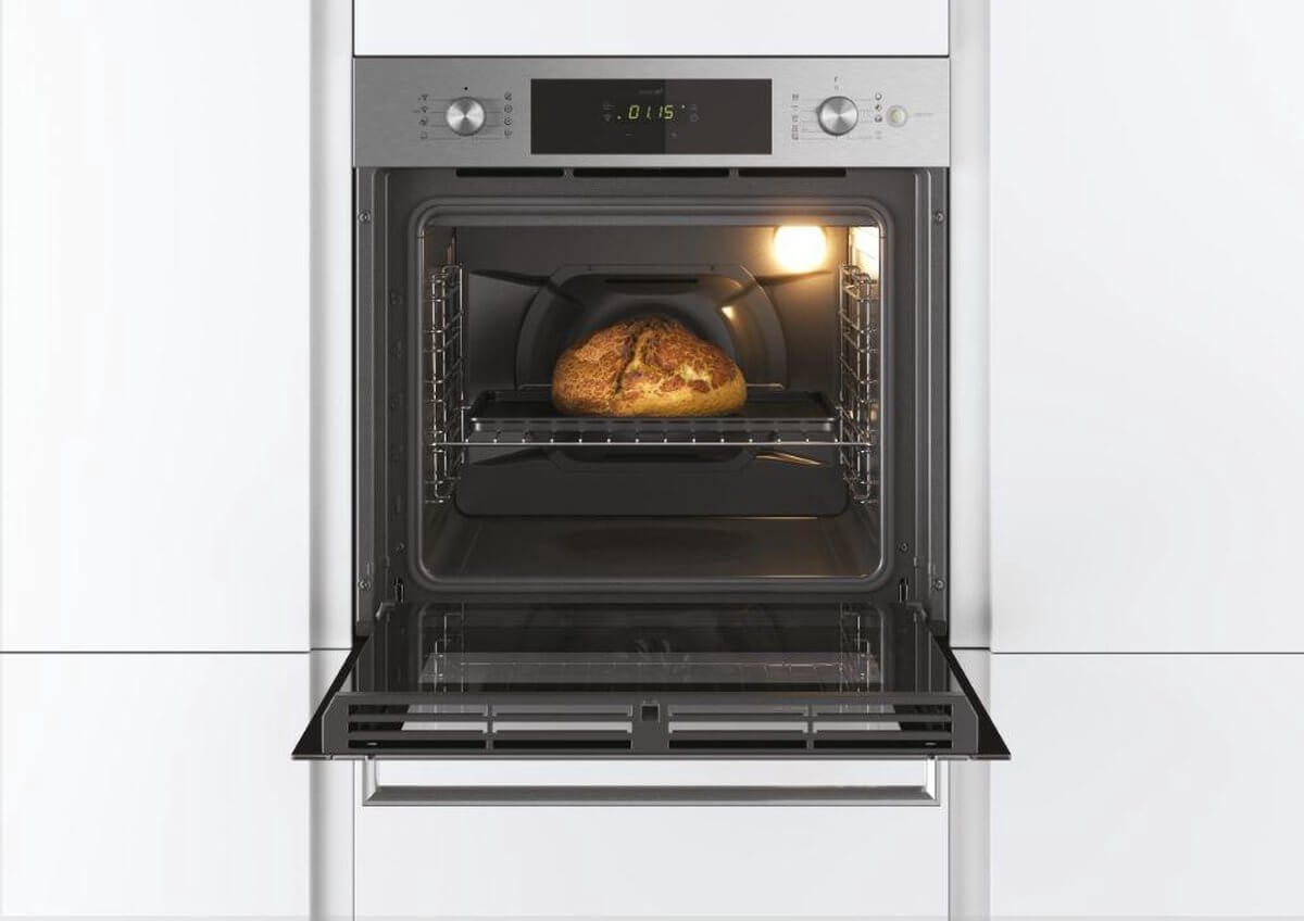 Frontaal zicht op de geopende Candy FCTS886X oven met binnenverlichting en vers brood.
