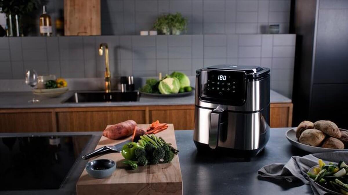 Electrolux E6AF1-4ST airfryer in keuken met donkergrijze tegels en diverse gerechten zoals kip, friet en zeevruchten.
