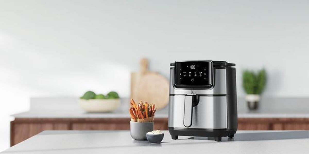 Electrolux E6AF1-4ST airfryer in roestvrij staal met touchscreen en bakje zoeteaardappelfriet naast kommetje saus.