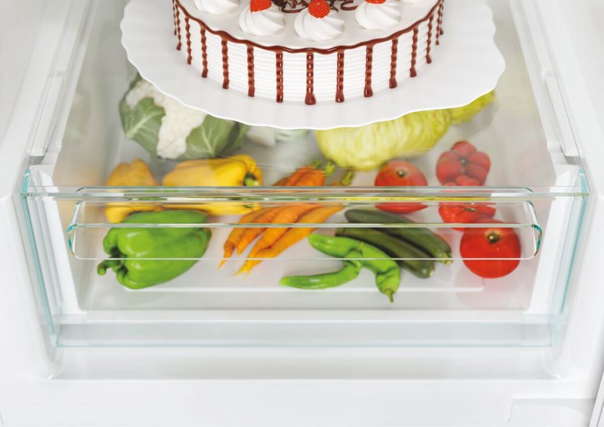 Groentelade koelkast met paprika’s, wortels, tomaten en bloemkool onder taart
