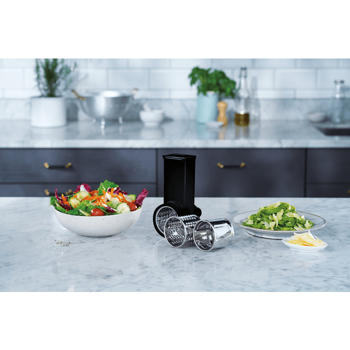 Groentesnijderaccessoire van de Electrolux EKM3700 naast kleurrijke salade en gesneden groenten
