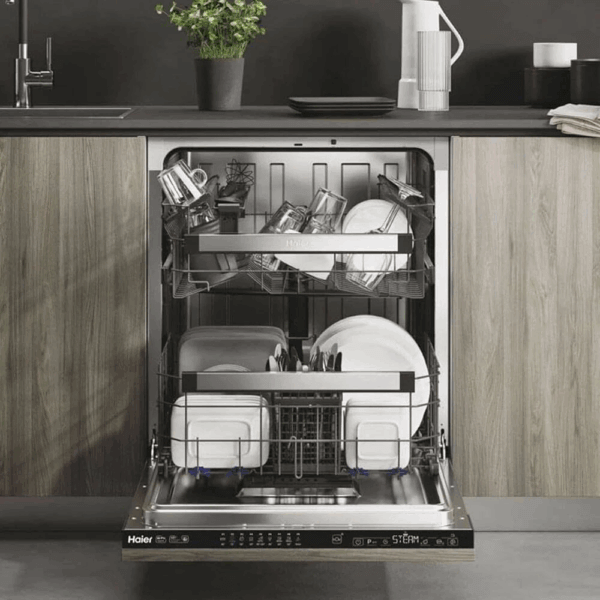 Volledig geïntegreerde Haier XI 6C3D0FB vaatwasser met open deur, gevuld met servies en glazen op drie niveaus, ingebouwd in moderne keuken met houten front en zwarte werkblad.
