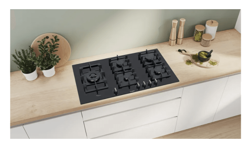 PPS9A6B90 (6) Table de cuisson gaz Bosch PPS9A6B90 encastrée dans un plan de travail en bois avec herbes et accessoires.